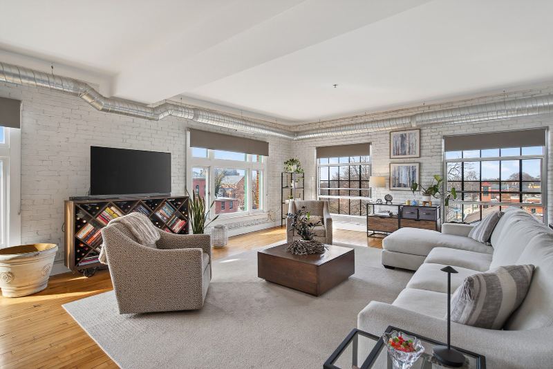 Living area with white-painted exposed brick, oversized factory windows and original hardwood floors